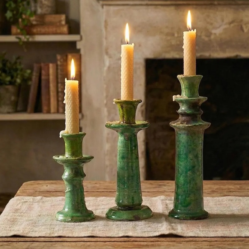 3 sizes of vintage green crackle ceramic candle holders (with lit candles) placed on a linen tablecloth, background with fireplace and bookshelf
